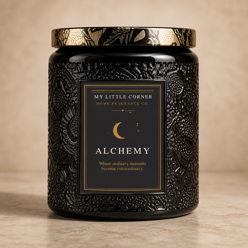 A black textured glass jar candle with a gold patterned lid and a black label featuring gold text that reads 'MY LITTLE CORNER HOME FRAGRANCES CO. ALCHEMY'.