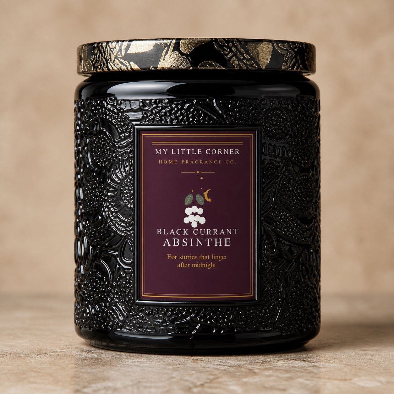 A black textured glass jar candle with a gold patterned lid and a dark burgundy label reading 'MY LITTLE CORNER HOME FRAGRANCE CO. BLACK CURRANT ABSINTHE'.