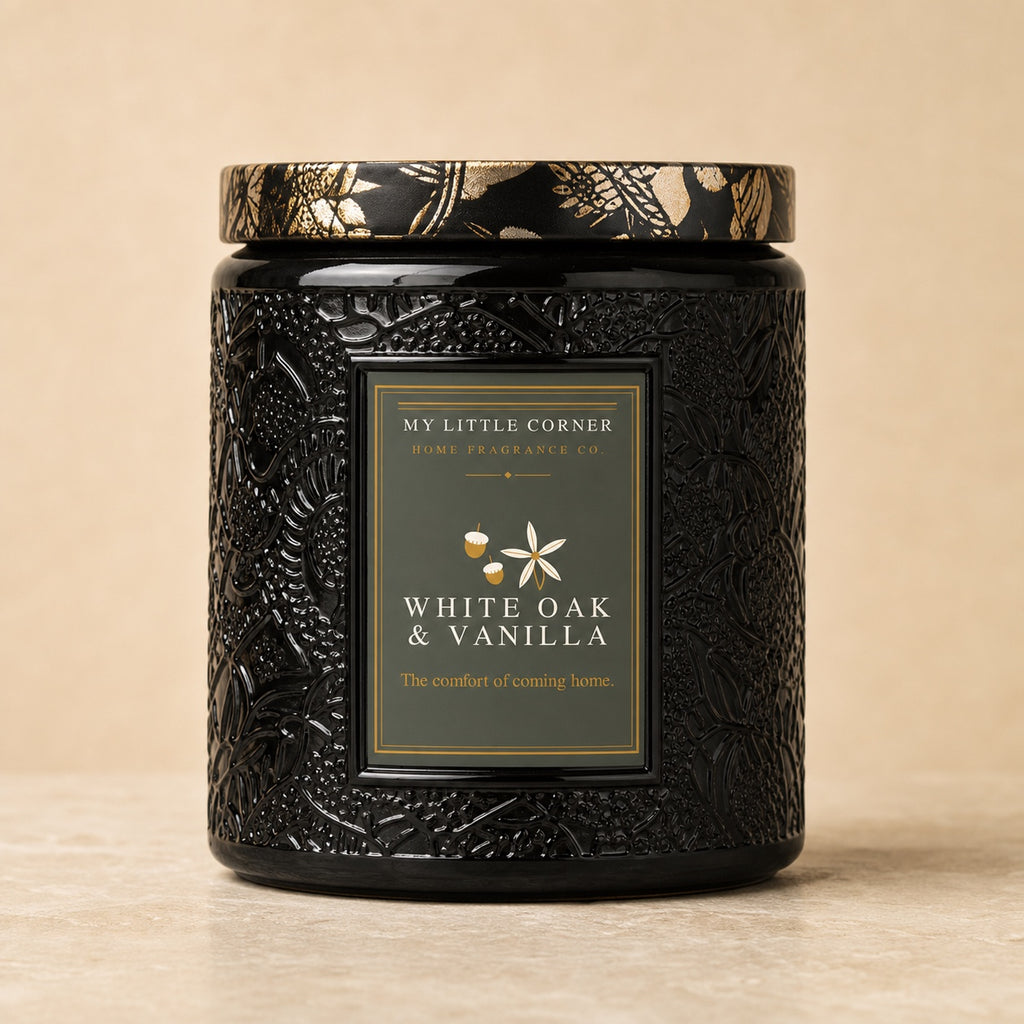 A black textured jar candle with a gold and black patterned lid, featuring a front label that reads 'MY LITTLE CORNER HOME FRAGRANCE CO. WHITE OAK & VANILLA'.