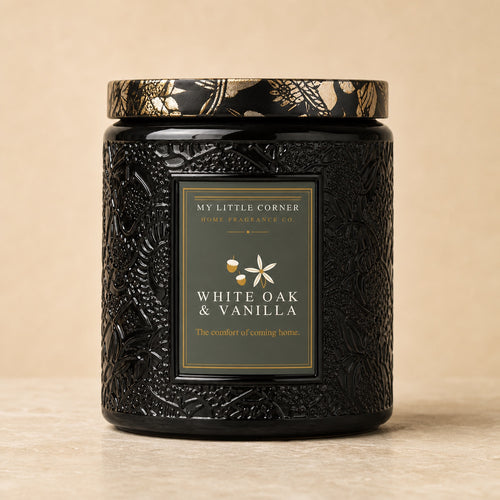 A black textured jar candle with a gold and black patterned lid, featuring a front label that reads 'MY LITTLE CORNER HOME FRAGRANCE CO. WHITE OAK & VANILLA'.